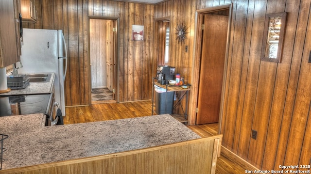 kitchen featuring wood finished floors, wood walls, brown cabinets, and electric stove