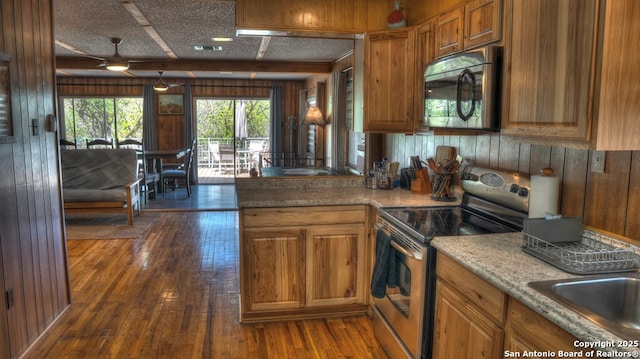 kitchen featuring stainless steel appliances, wooden walls, a ceiling fan, brown cabinetry, and dark wood-style flooring
