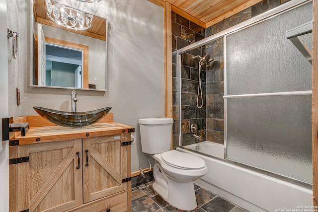 bathroom with vanity, a textured wall, baseboards, toilet, and shower / bath combination with glass door