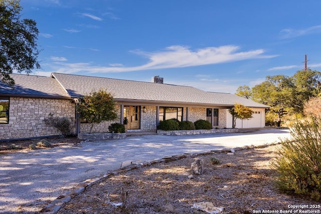 ranch-style home featuring an attached garage, a porch, driveway, and a chimney