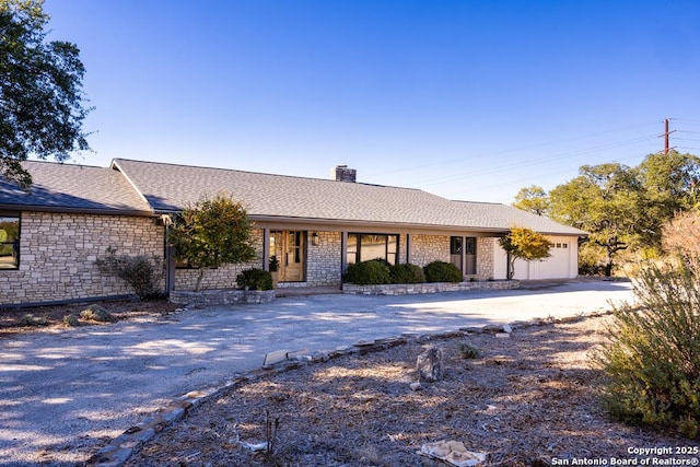 ranch-style house featuring a chimney, aphalt driveway, an attached garage, a porch, and roof with shingles