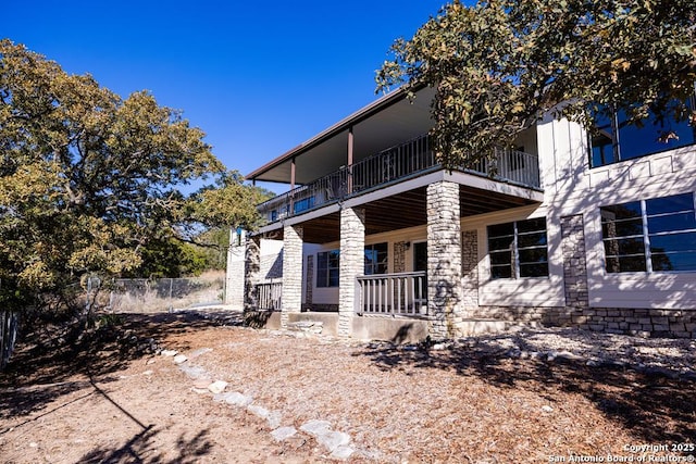 rear view of house featuring covered porch, a balcony, and fence