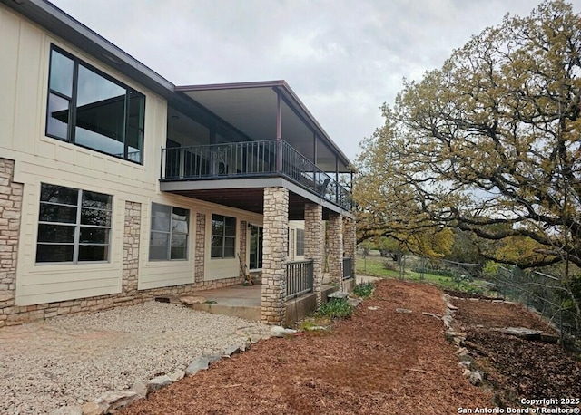 view of side of home with fence, a patio, stone siding, and a balcony
