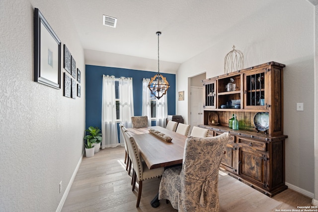 dining space featuring light wood-type flooring, baseboards, visible vents, a notable chandelier, and a textured wall