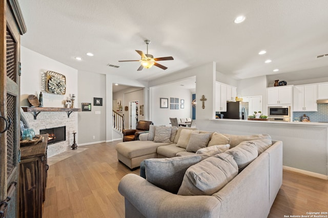 living room with visible vents, a ceiling fan, a stone fireplace, and light wood finished floors