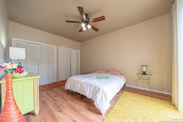 bedroom with baseboards, wood finished floors, two closets, and ceiling fan