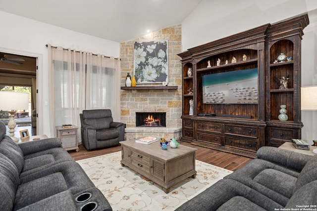 living room with lofted ceiling, a ceiling fan, a stone fireplace, and light wood finished floors