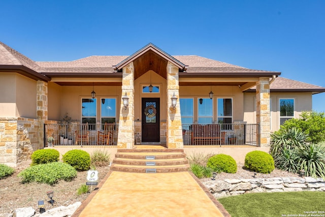 view of exterior entry with stucco siding, roof with shingles, a porch, and stone siding