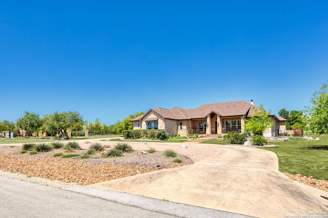 ranch-style house featuring a chimney, curved driveway, covered porch, stone siding, and a front yard