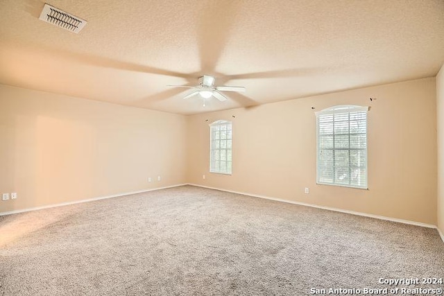 carpeted empty room with a textured ceiling, visible vents, a ceiling fan, and baseboards