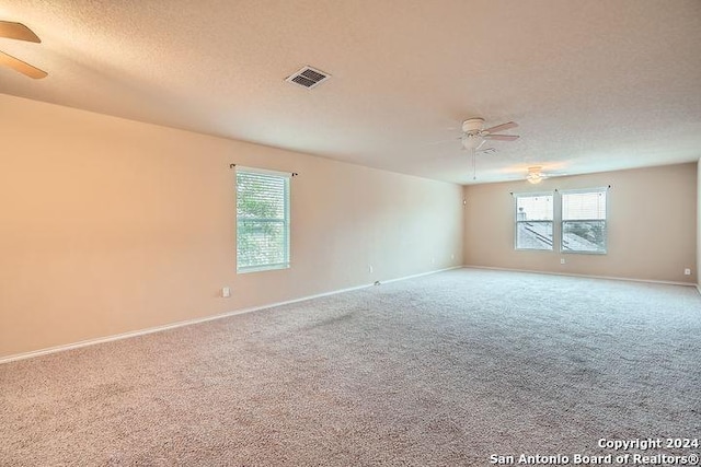 carpeted empty room featuring baseboards, a ceiling fan, visible vents, and a textured ceiling