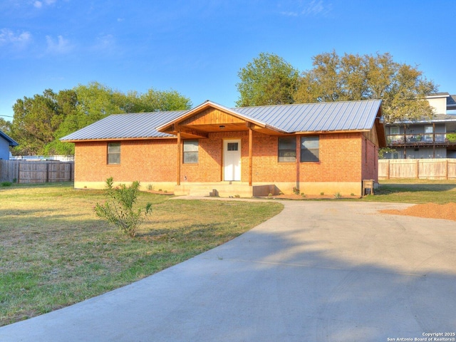 view of front of house with a front lawn, driveway, fence, metal roof, and brick siding