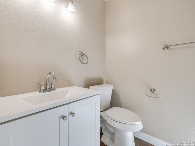 half bathroom featuring baseboards, wood finished floors, vanity, and toilet