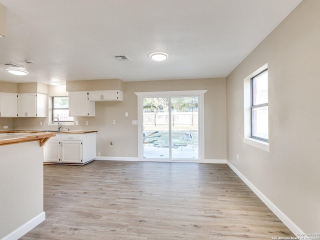 kitchen featuring white cabinets, visible vents, a sink, light wood-style floors, and a wealth of natural light