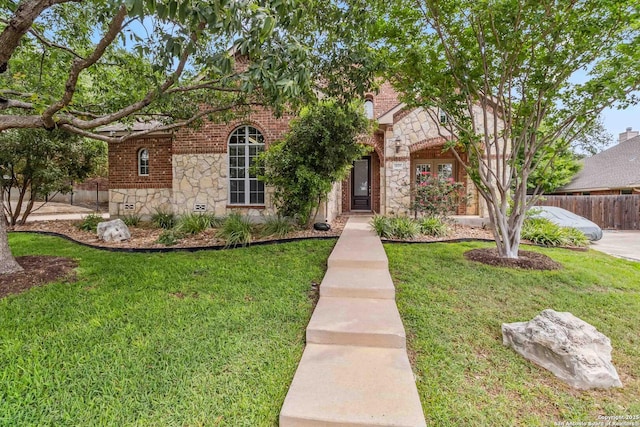view of front of house featuring brick siding, stone siding, a front yard, and fence