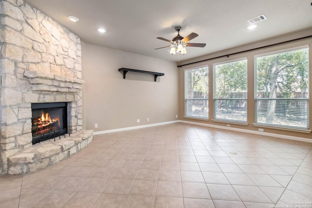unfurnished living room with light tile patterned floors, a stone fireplace, visible vents, and ceiling fan