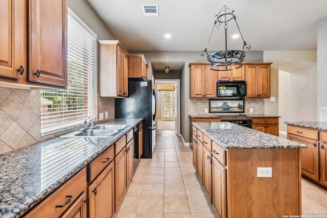 kitchen featuring a sink, black appliances, stone countertops, visible vents, and a kitchen island