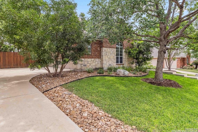 obstructed view of property with concrete driveway, a front lawn, fence, and stone siding