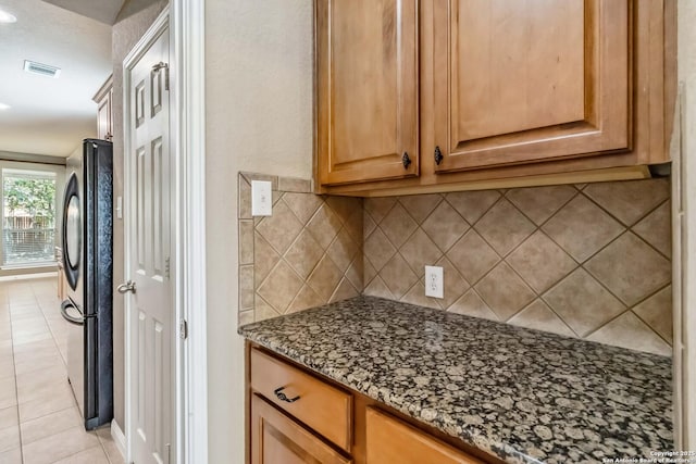 kitchen with dark stone counters, visible vents, freestanding refrigerator, decorative backsplash, and light tile patterned floors