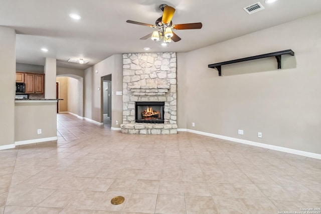 unfurnished living room with arched walkways, visible vents, a ceiling fan, a fireplace, and light tile patterned floors