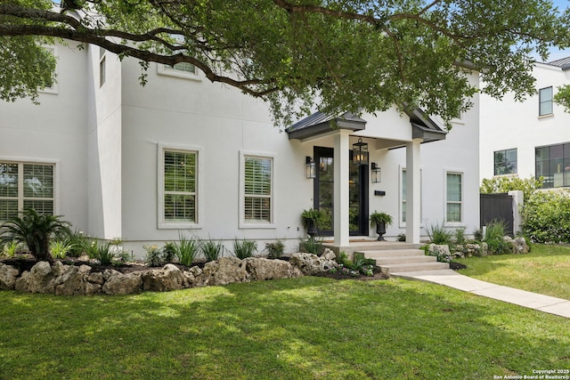 view of front facade with metal roof, a standing seam roof, a front lawn, and stucco siding