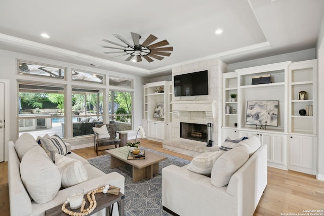living room featuring a fireplace, light wood-type flooring, a ceiling fan, and ornamental molding