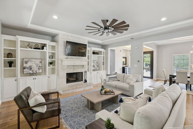 living area with a ceiling fan, wood finished floors, a stone fireplace, and ornamental molding