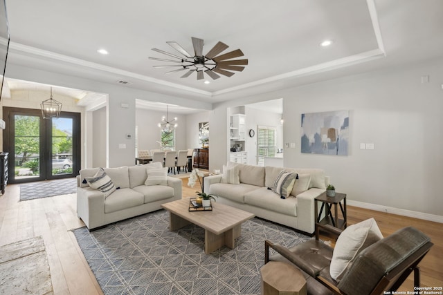 living room with an inviting chandelier, a healthy amount of sunlight, hardwood / wood-style floors, and a raised ceiling