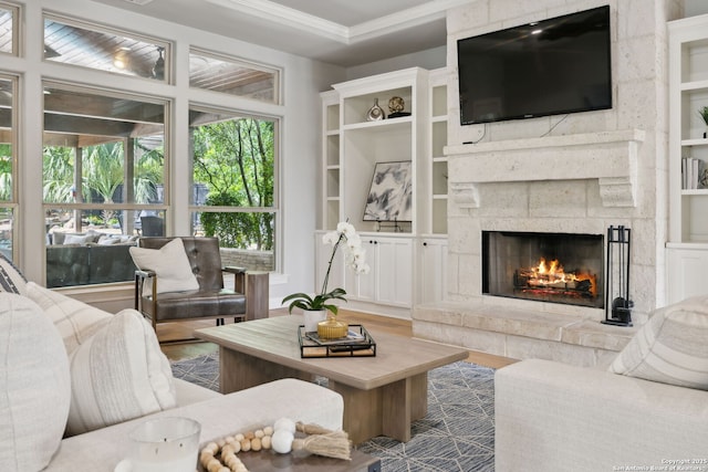 living area featuring built in shelves, ornamental molding, a lit fireplace, and wood finished floors