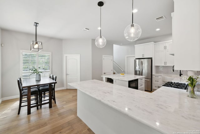 kitchen with light wood finished floors, light stone countertops, visible vents, and stainless steel fridge