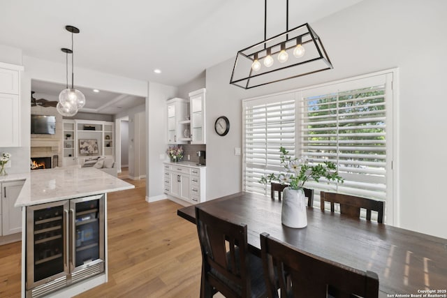 dining room with recessed lighting, beverage cooler, light wood finished floors, a lit fireplace, and a chandelier