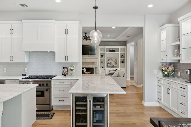 kitchen featuring white cabinets, a peninsula, visible vents, high end stove, and beverage cooler