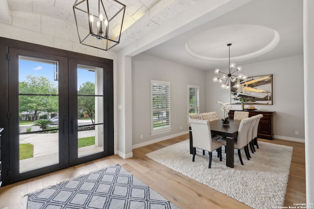 dining space featuring french doors, wood finished floors, a notable chandelier, and a raised ceiling