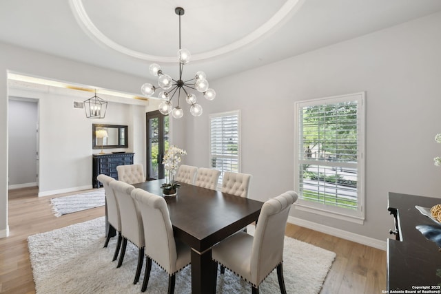 dining area with an inviting chandelier, a tray ceiling, light wood finished floors, and baseboards