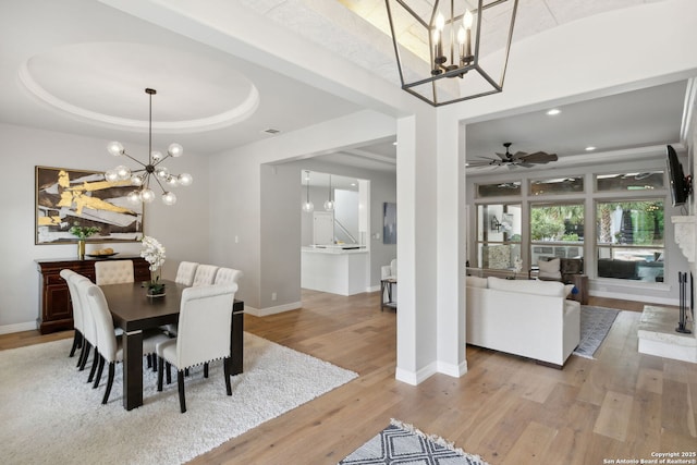 dining room featuring ceiling fan with notable chandelier, light wood-style flooring, baseboards, visible vents, and a raised ceiling