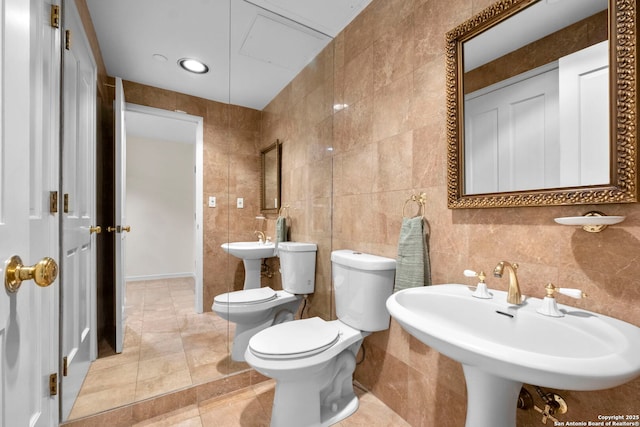 bathroom with toilet, tile patterned floors, a sink, and tile walls