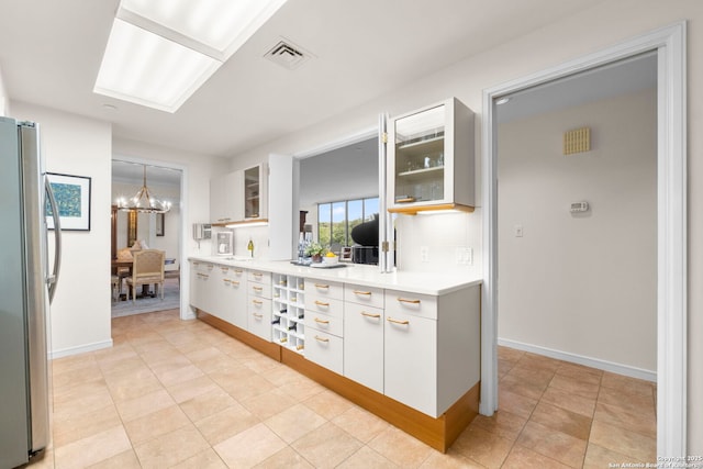 kitchen featuring visible vents, freestanding refrigerator, a notable chandelier, glass insert cabinets, and light countertops