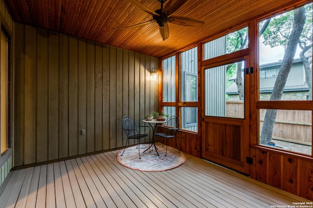 sunroom / solarium with wood-type flooring, wooden walls, a ceiling fan, and a deck