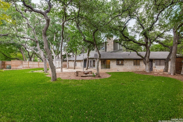 back of house with a lawn, a chimney, fence, and stone siding