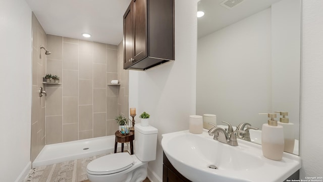 bathroom featuring toilet, vanity, visible vents, and tiled shower