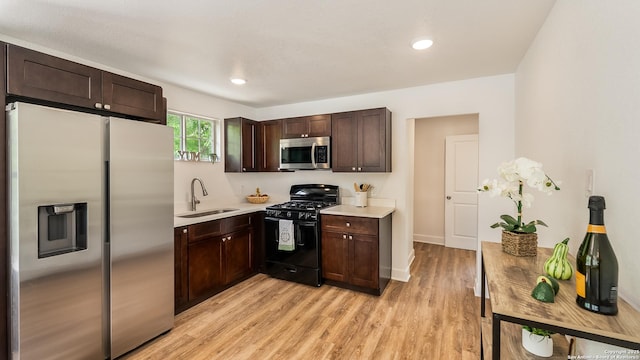 kitchen featuring stainless steel appliances, a sink, dark brown cabinetry, light wood-style floors, and light countertops