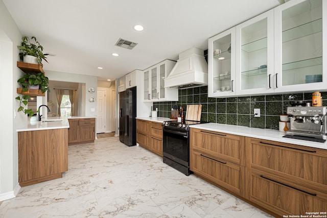 kitchen with brown cabinets, a sink, custom range hood, visible vents, and black appliances