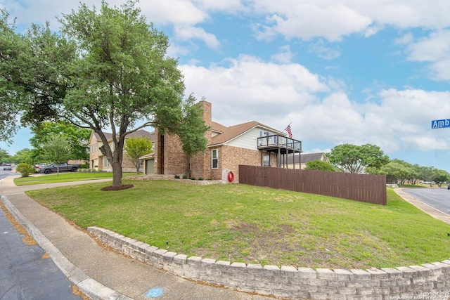 view of side of home with fence, a balcony, a chimney, brick siding, and a lawn