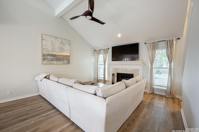 living area featuring vaulted ceiling with beams, baseboards, a tiled fireplace, and wood finished floors