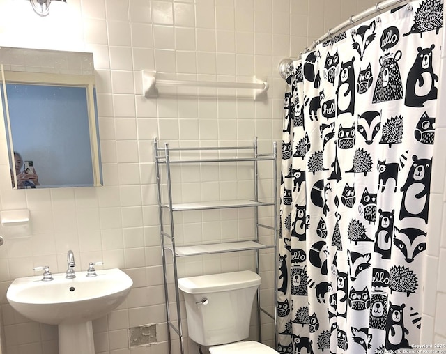 bathroom featuring tile walls, a sink, curtained shower, and toilet