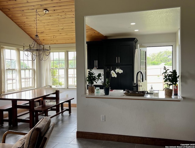 kitchen featuring tile patterned floors, dark cabinetry, a sink, baseboards, and a notable chandelier