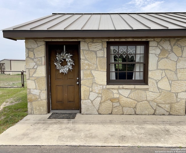 view of exterior entry featuring a standing seam roof, fence, stone siding, and metal roof