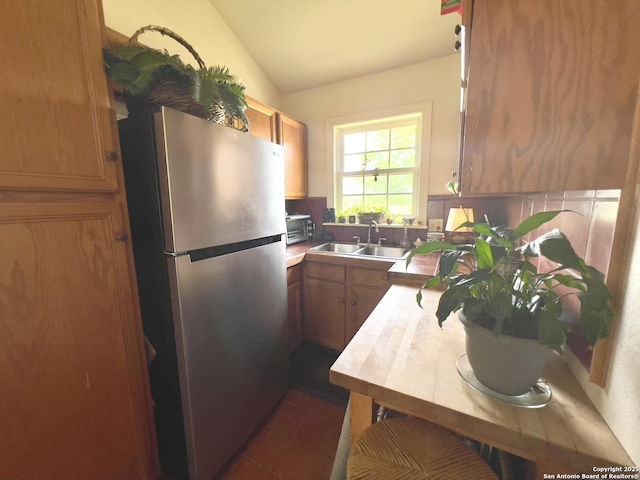 kitchen featuring vaulted ceiling, a sink, dark tile patterned flooring, brown cabinetry, and freestanding refrigerator