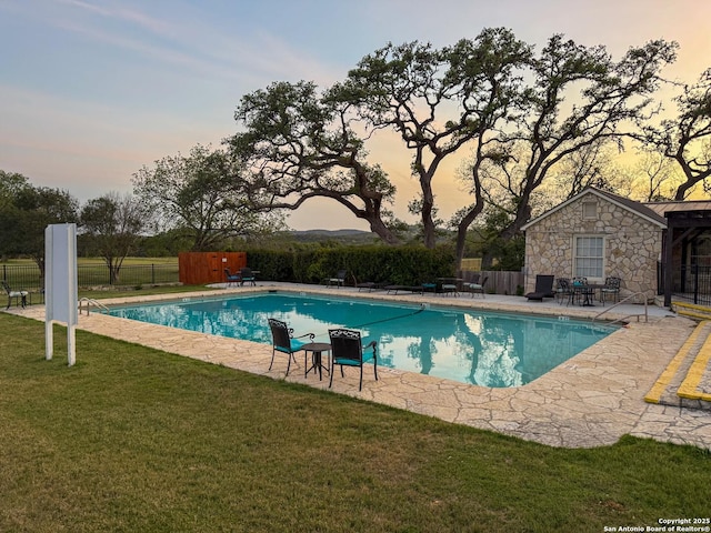 pool at dusk with fence, a lawn, a fenced in pool, and a patio area