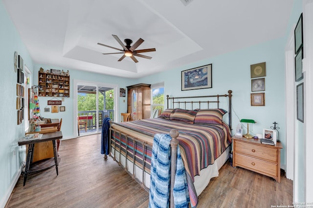 bedroom with ceiling fan, wood finished floors, a tray ceiling, and access to exterior